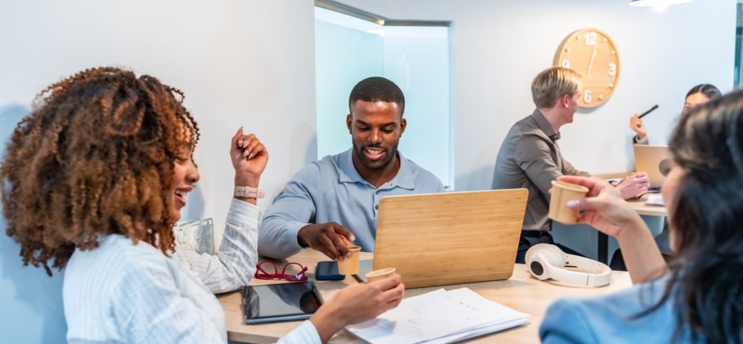 Diverse team working together in a coworking space, using laptop and drinking coffee, enjoying a productive and collaborative work environment
