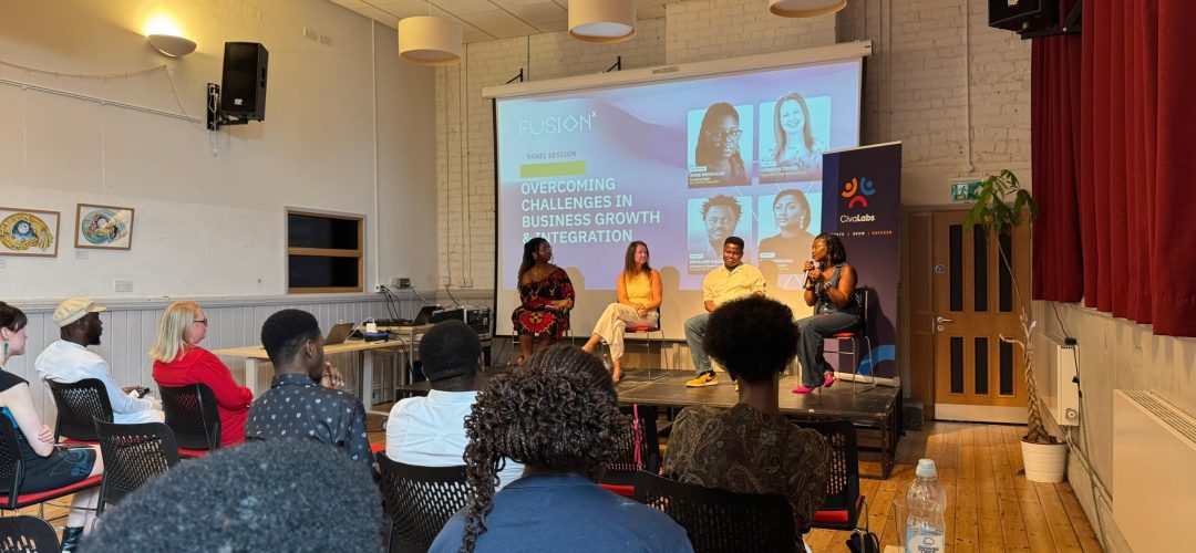 Panelists sitting on a stage.Audience members can be seen